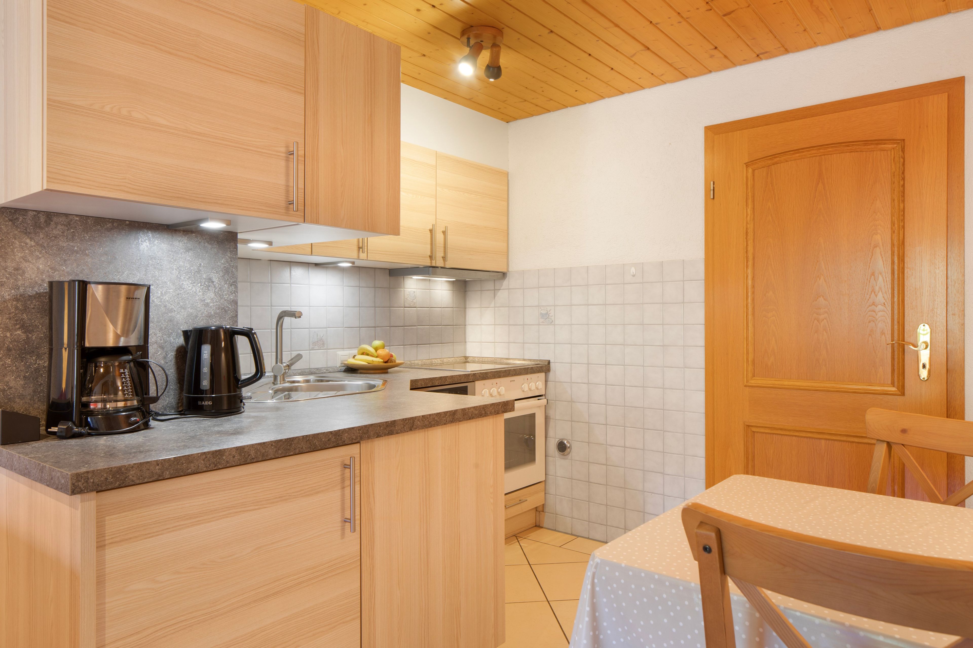 Een functionele keuken met houten kastjes, een koffiezetapparaat, een spoelbak en een kookplaat.