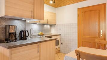 Een functionele keuken met houten kastjes, een koffiezetapparaat, een spoelbak en een kookplaat.