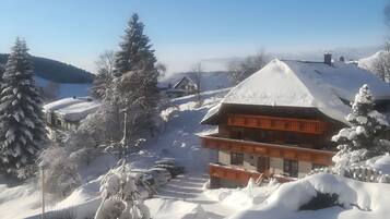 Ein mit Schnee bedecktes Chalet mit einem markanten Balkon und freiem Blick auf die verschneite Landschaft.
