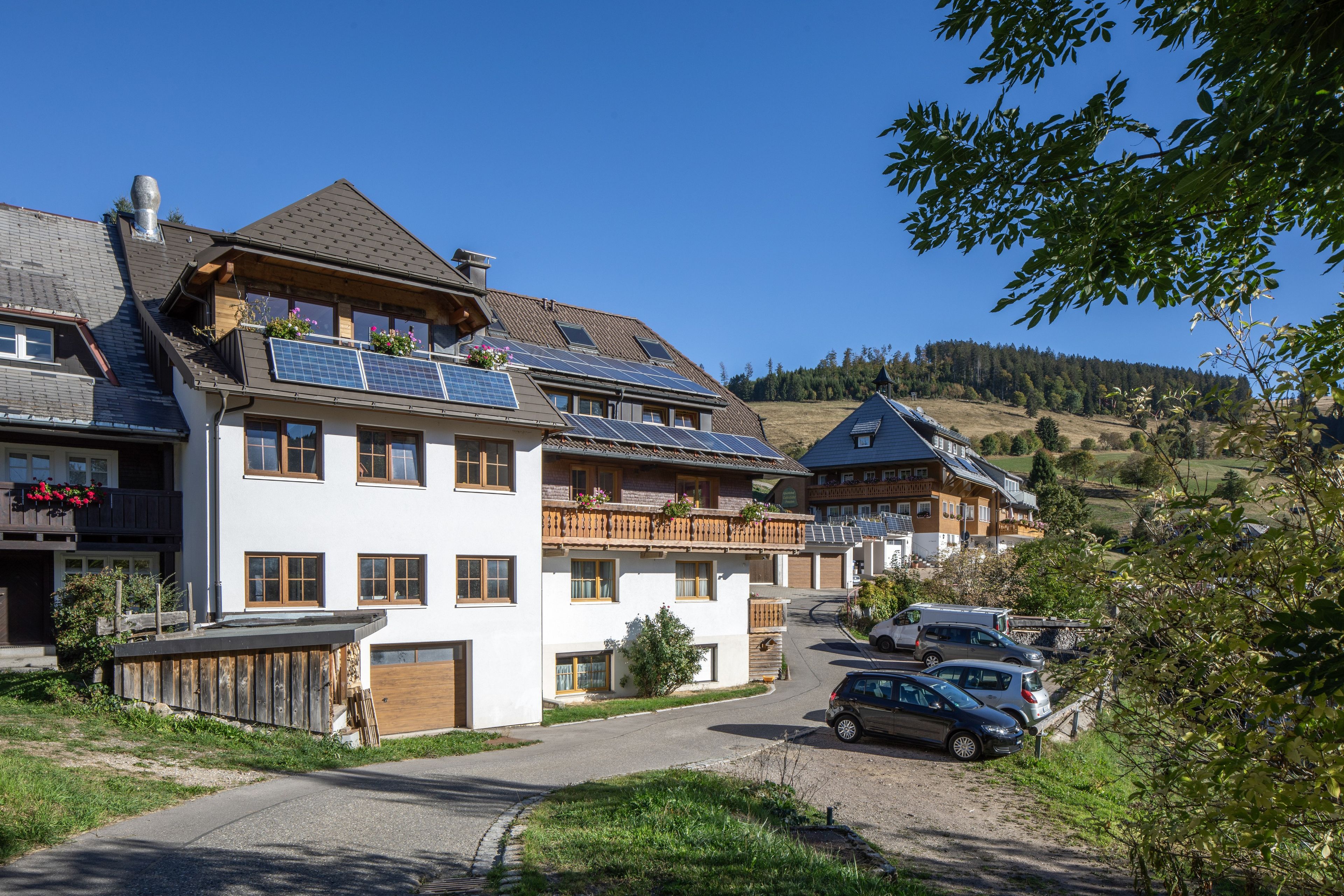 Eine Reihe traditioneller europäischer Gebäude mit Solaranlagen, einer gepflasterten Auffahrt und einem geparkten Auto davor.