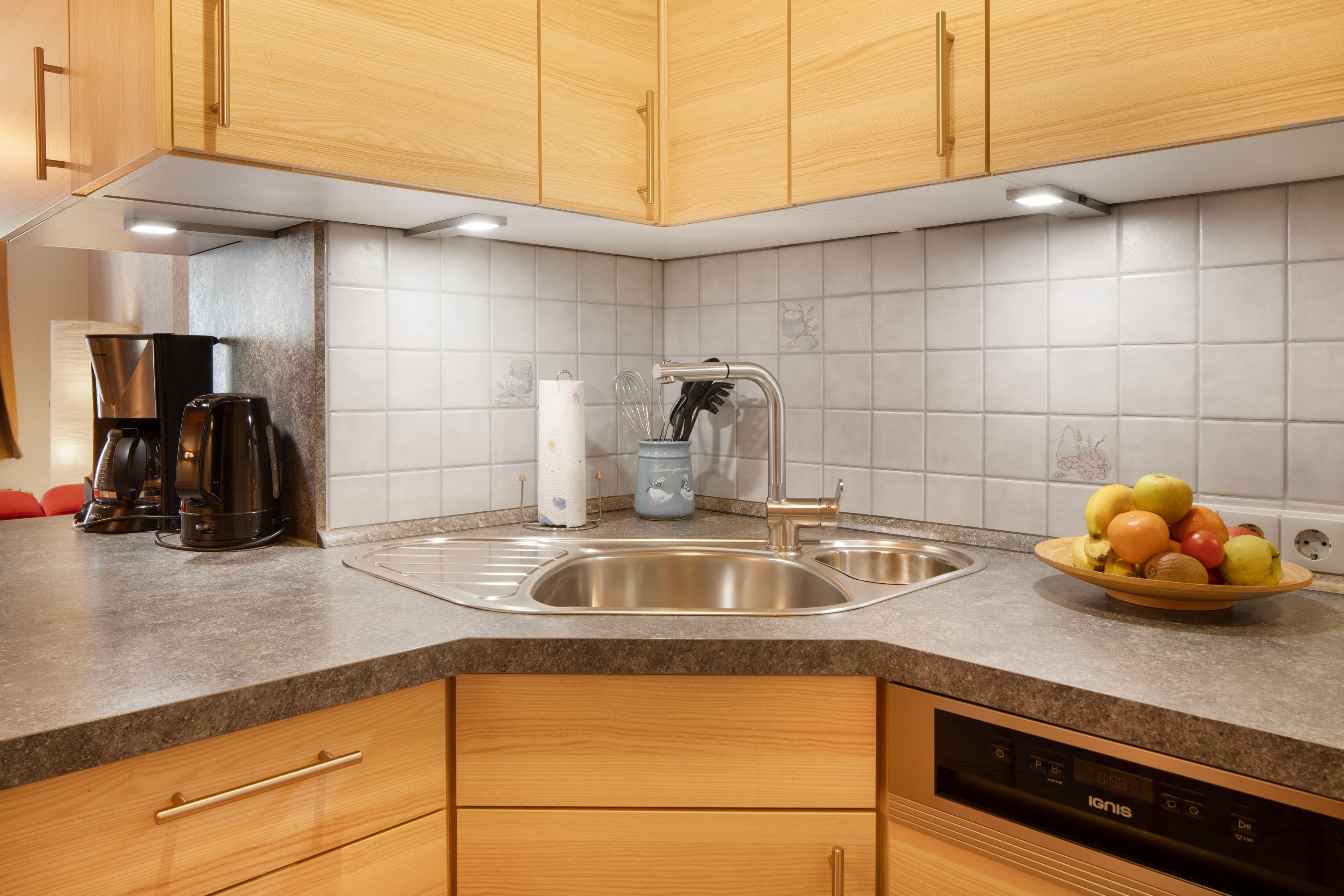 Een moderne keuken met houten kastjes, een roestvrijstalen spoelbak, een koffiezetapparaat en een fruitschaal op het aanrecht.
