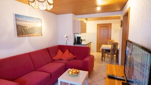 A living room with a red sofa, a small table with fruit, a TV, and a kitchen in the background. - Apartment 1 at Bühlhof in Todtnauberg (Todtnau)