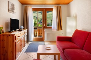 Un salón acogedor con un sofá rojo, armarios de madera, un televisor y vistas a un paisaje verde a través de un ventanal.