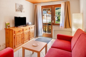 A room with a television, wooden cabinet, red sofa, and a view of a green landscape through a window. - Bühlhof Todtnauberg Apartment 1 (Todtnau)