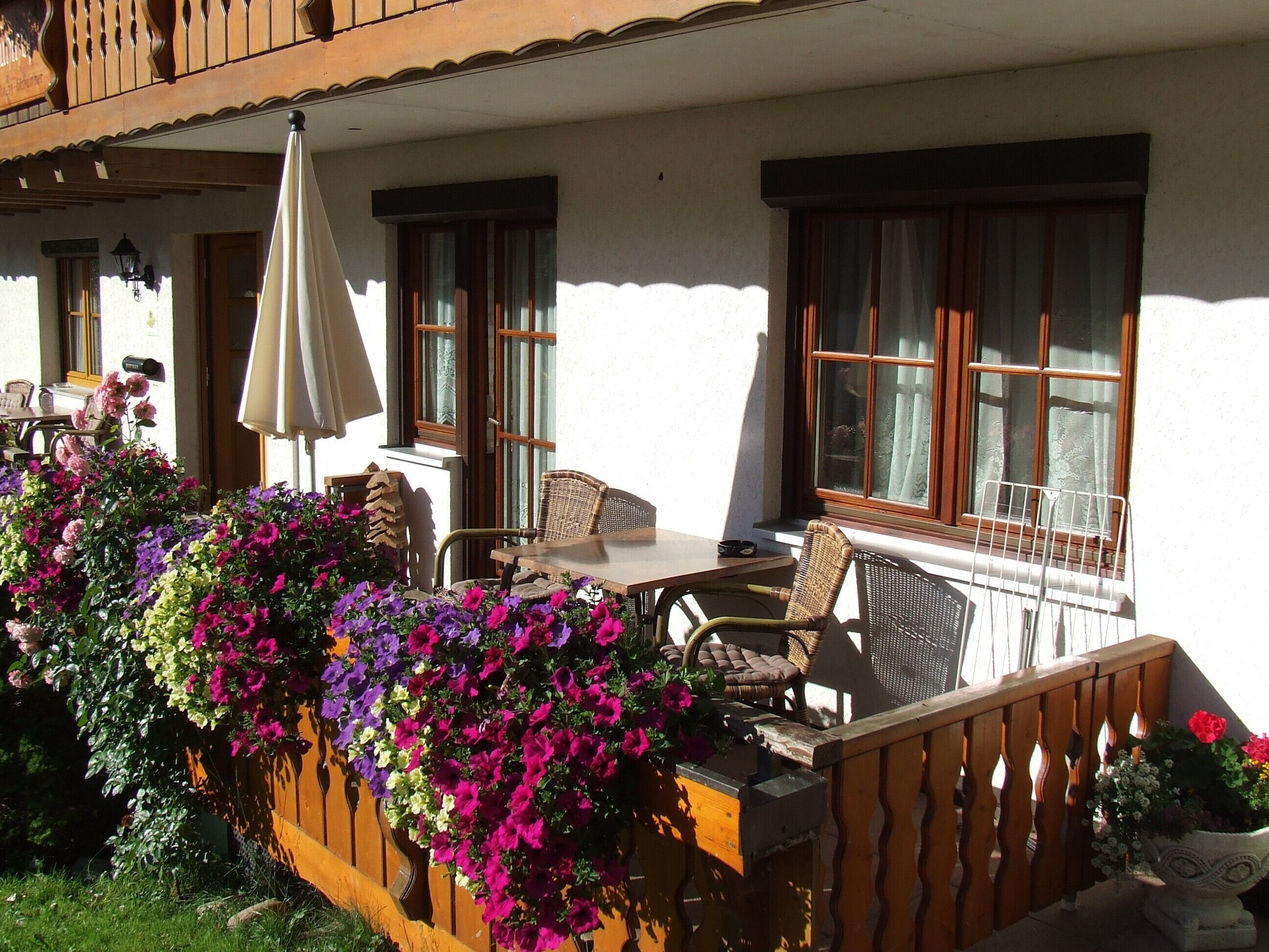 Une terrasse avec une table et des chaises, une clôture en bois ornée de fleurs et un bâtiment doté de fenêtres et d’un balcon.