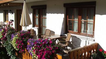 Une terrasse avec une table et des chaises, une clôture en bois ornée de fleurs et un bâtiment doté de fenêtres et d’un balcon.