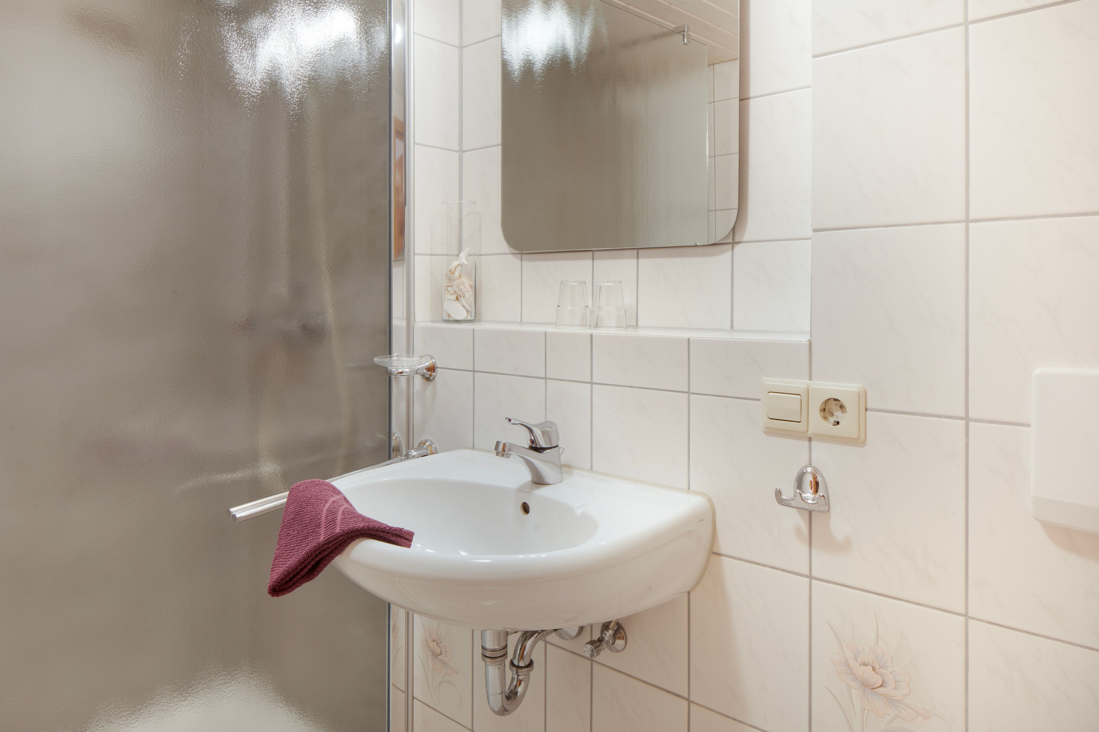 Un baño con un lavamanos blanco, un espejo encima y una toalla colgada en la pared.