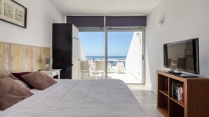 A hotel room with a bed, a television, a bookshelf, and a balcony with a view of the sea. - Apartment in Las Palmas by Las Canteras Beach (Las Palmas de Gran Canaria)