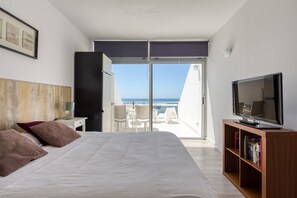 A hotel room with a bed, a television, a bookshelf, and a balcony with a view of the sea. - Apartment in Las Palmas by Las Canteras Beach (Las Palmas de Gran Canaria)