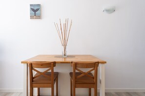 A wooden table with two chairs, a clear vase with sticks, a wall-mounted light, and a poster on the wall. - Apartment in Las Palmas by Las Canteras Beach (Las Palmas de Gran Canaria)