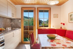A modern kitchen with a sink, a fruit bowl, and a dining area with a table and red seating. - Bühlhof Todtnauberg Apartment 3 (Todtnau)