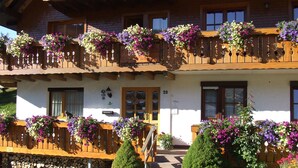 Un edificio a due piani con un balcone in legno, il numero '20' ben visibile sulla porta e fioriere sulle ringhiere del balcone.