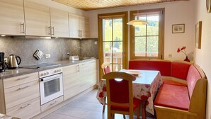 Una cucina con piano cottura, forno e lavello, un tavolo da pranzo con sedie e una panca con tovaglia a fiori.