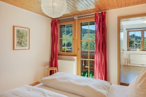 A bedroom with a bed, a window with curtains, a radiator, and a painting on the wall. - Bühlhof Todtnauberg Apartment 3 (Todtnau)