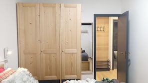 A bedroom with a large wardrobe, a bed with a fluffy white cover, and a visible bathroom with a towel rack. - Apricola By ca-sa check (Aprica)