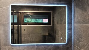 A bathroom with a built-in television screen, a towel rack, and a shower area. - Apricola By ca-sa check (Aprica)