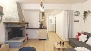 A modern living room with a fireplace, a sofa, a coffee table, and a kitchen area in the background. - Apricola By ca-sa check (Aprica)