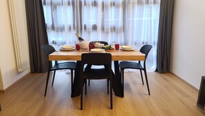 A dining area with a wooden table, black chairs, and a window with sheer curtains. - Apricola By ca-sa check (Aprica)