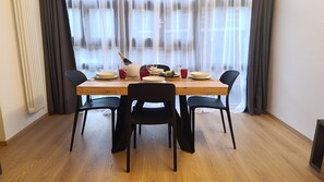 A dining area with a wooden table, black chairs, and a window with sheer curtains. - Apricola By ca-sa check (Aprica)