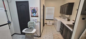 A compact kitchen with a washing machine, a small sink, and a child's potty chair. - 11 Luxury Acres Retreat, Pool, Fishing, Sleeps 14-24 (Mabank)