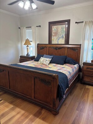 A bedroom with a wooden bed, a nightstand, a lamp, a window with curtains, and a ceiling fan. - 11 Luxury Acres Retreat, Pool, Fishing, Sleeps 14-24 (Mabank)