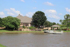 A house with a dock extending into a body of water, surrounded by trees and a clear sky. - 11 Luxury Acres Retreat, Pool, Fishing, Sleeps 14-24 (Mabank)