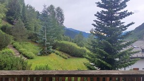 Eine Berglandschaft mit einer Holzdiele, die auf eine Wiese mit Bäumen und ein Gebäude mit Ziegeldach blickt.