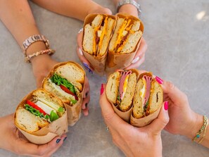 Four sandwiches held by hands with visible fillings. - Luz Suit (Kaş)
