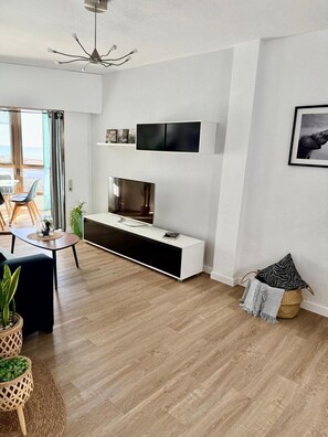 A modern living room with a TV, wooden flooring, and a view of the outdoors. - Sea View Apartment with Pool in Almería for up to 4 Guests (Retamar)