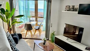 A modern living room with a sofa, a coffee table, a TV, and a dining area with chairs and a table. - Sea View Apartment with Pool in Almería for up to 4 Guests (Retamar)