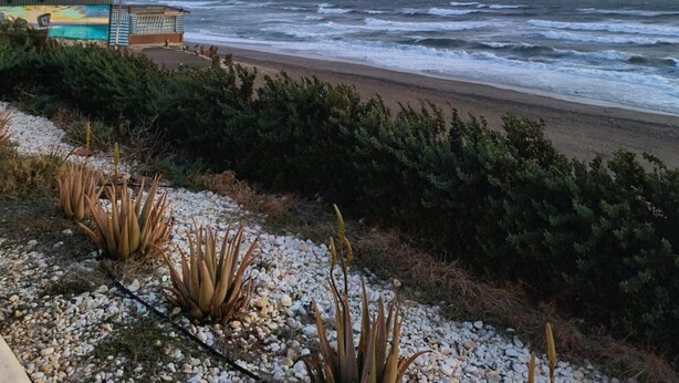 A coastal view with a beach, rocky foreground, and a building with a colorful mural. - Sea View Apartment with Pool in Almería for up to 4 Guests (Retamar)