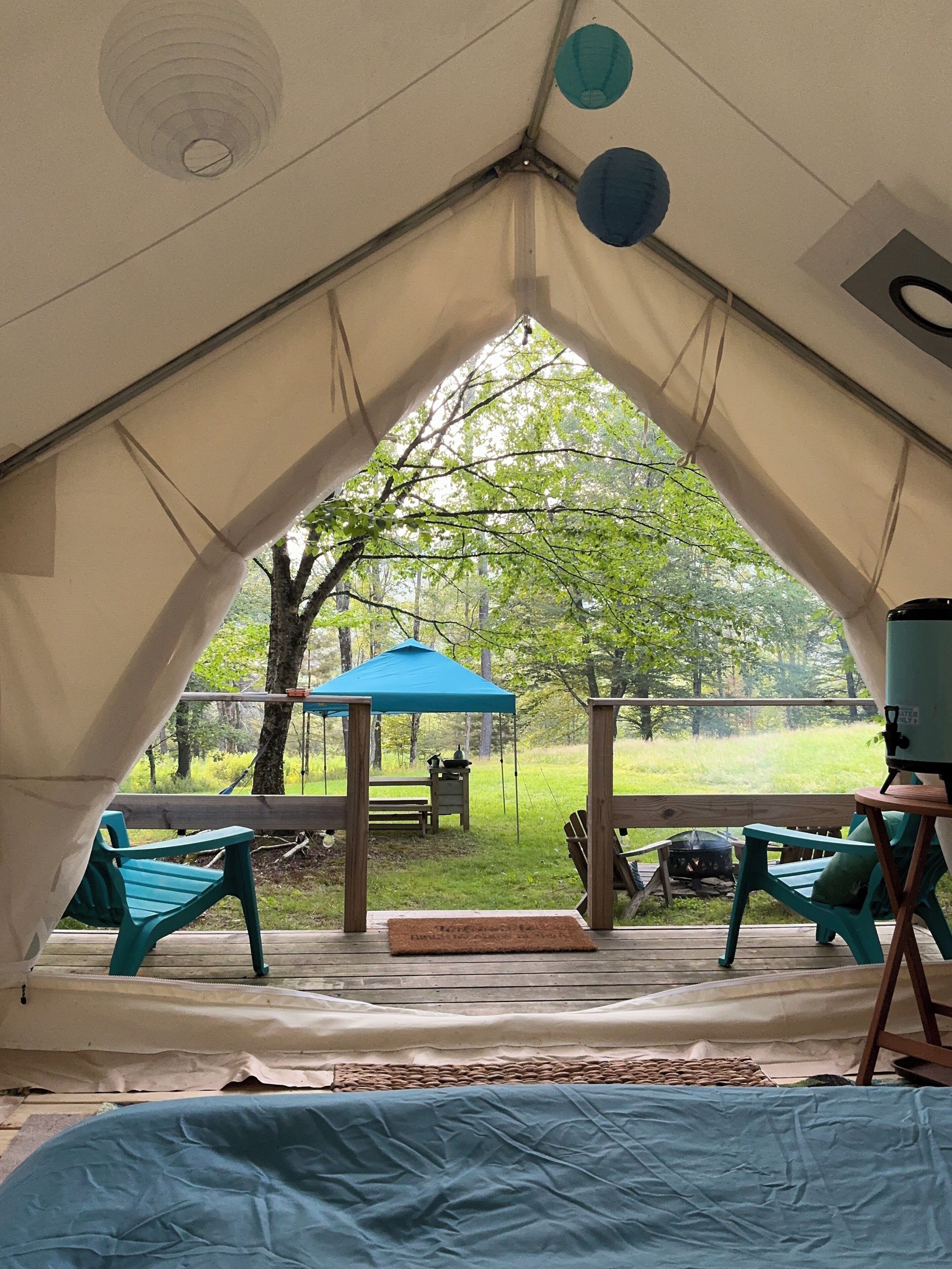 A tent with a view of a grassy area, a blue canopy, and outdoor furniture.