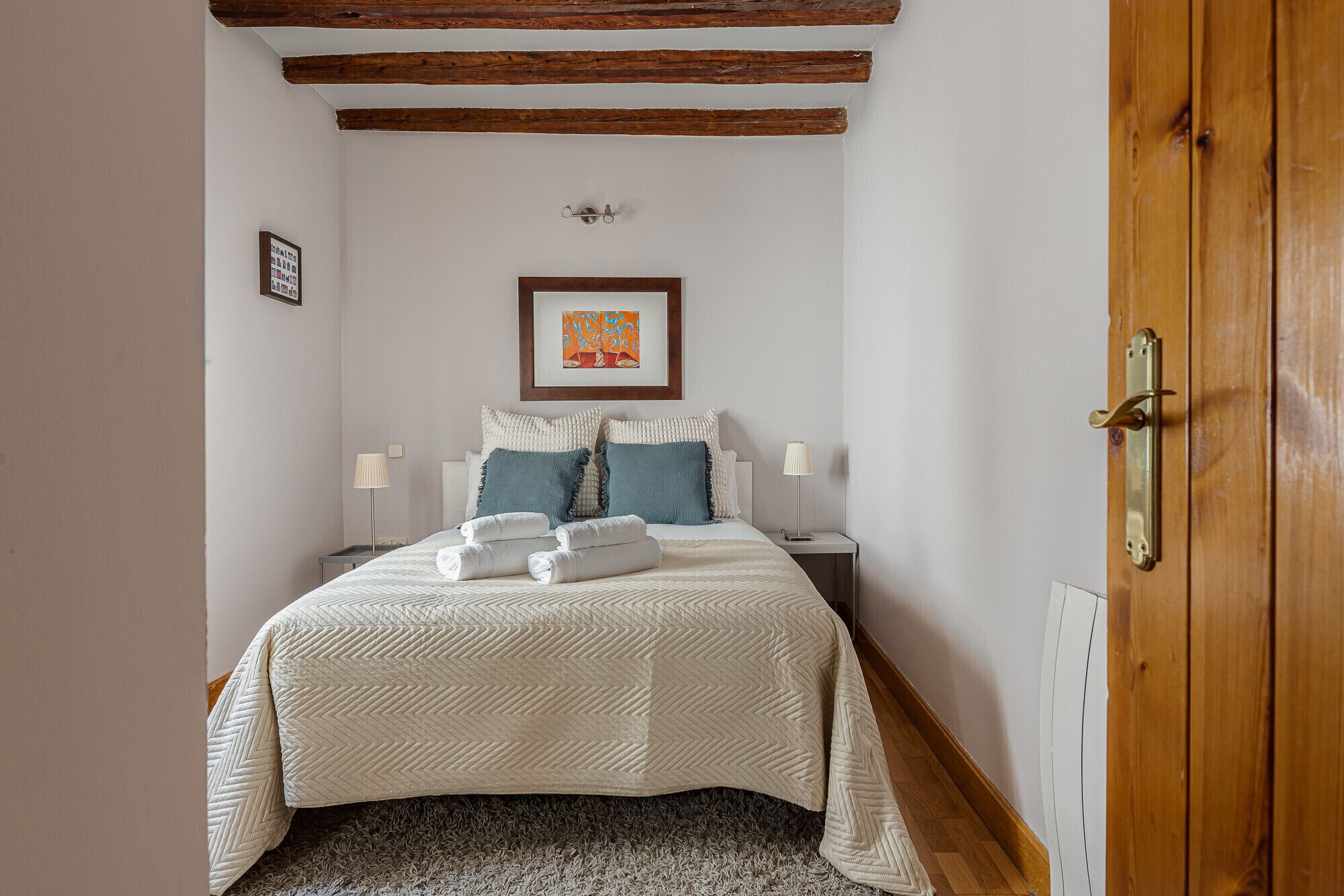 A bedroom with a bed, two bedside tables, a wooden door, and a framed picture on the wall.