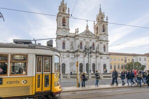 A tram with 'carris' branding, a historic building with two towers, and a group of people on the sidewalk. - Studio 'Madragoa Cozy Studio' (Lisbon)