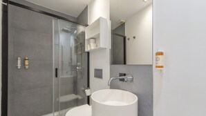 Ett modernt badrum med en dusch som är avskärmad med glasväggar, en vit toalett och ett stort, vitt handfat.