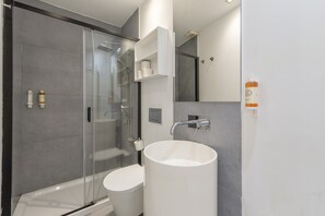 Ein modernes Badezimmer mit einer gläsernen Duschkabine, einer weißen Toilette und einem großen weißen Waschbecken.