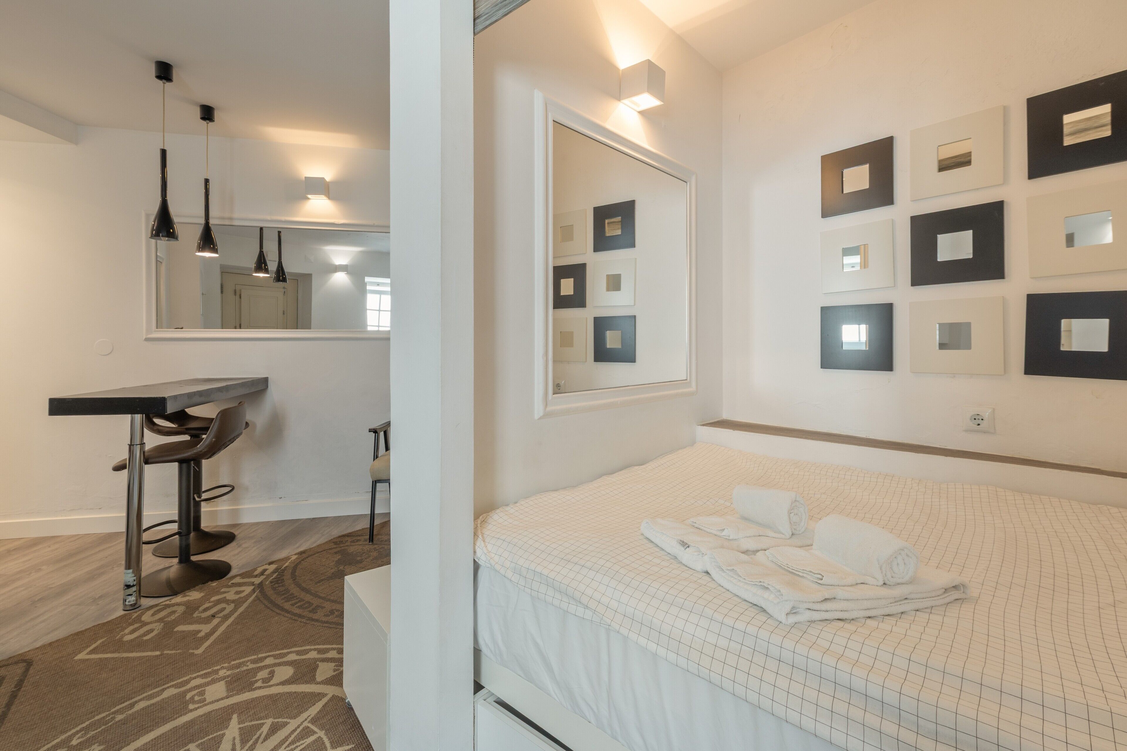 A hotel room with a bed, a desk, a chair, a mirror, and wall-mounted picture frames.