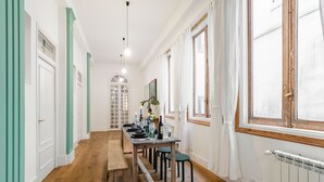 A long dining table with chairs, a bench, and a window with curtains. - Waou Gran Via IX - Short-Term Rental (Madrid)