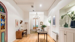 A spacious hallway with a wooden floor, a chandelier, and a dining area with a table and chairs. - Waou Gran Via IX - Short-Term Rental (Madrid)
