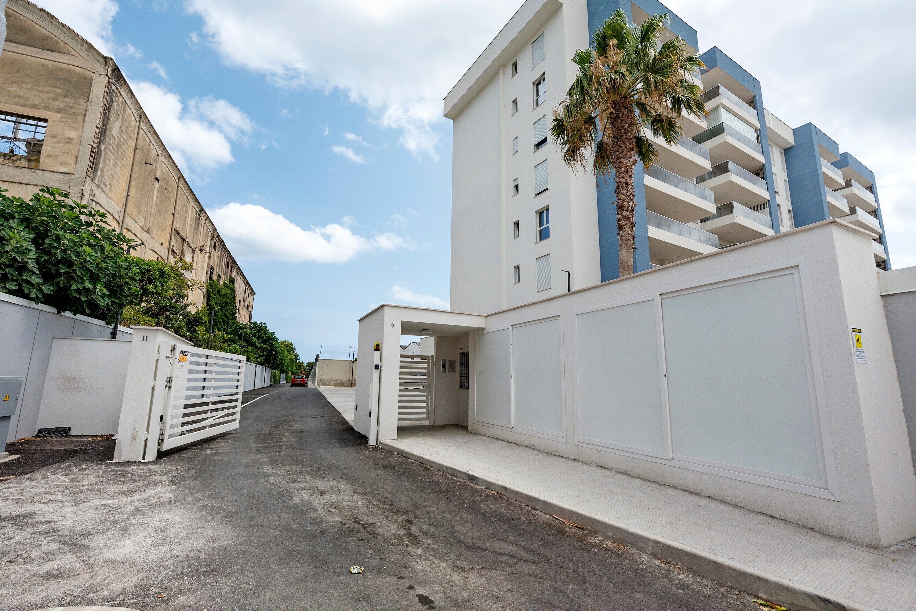 Una strada con un cancello, un edificio moderno con balconi e una palma.