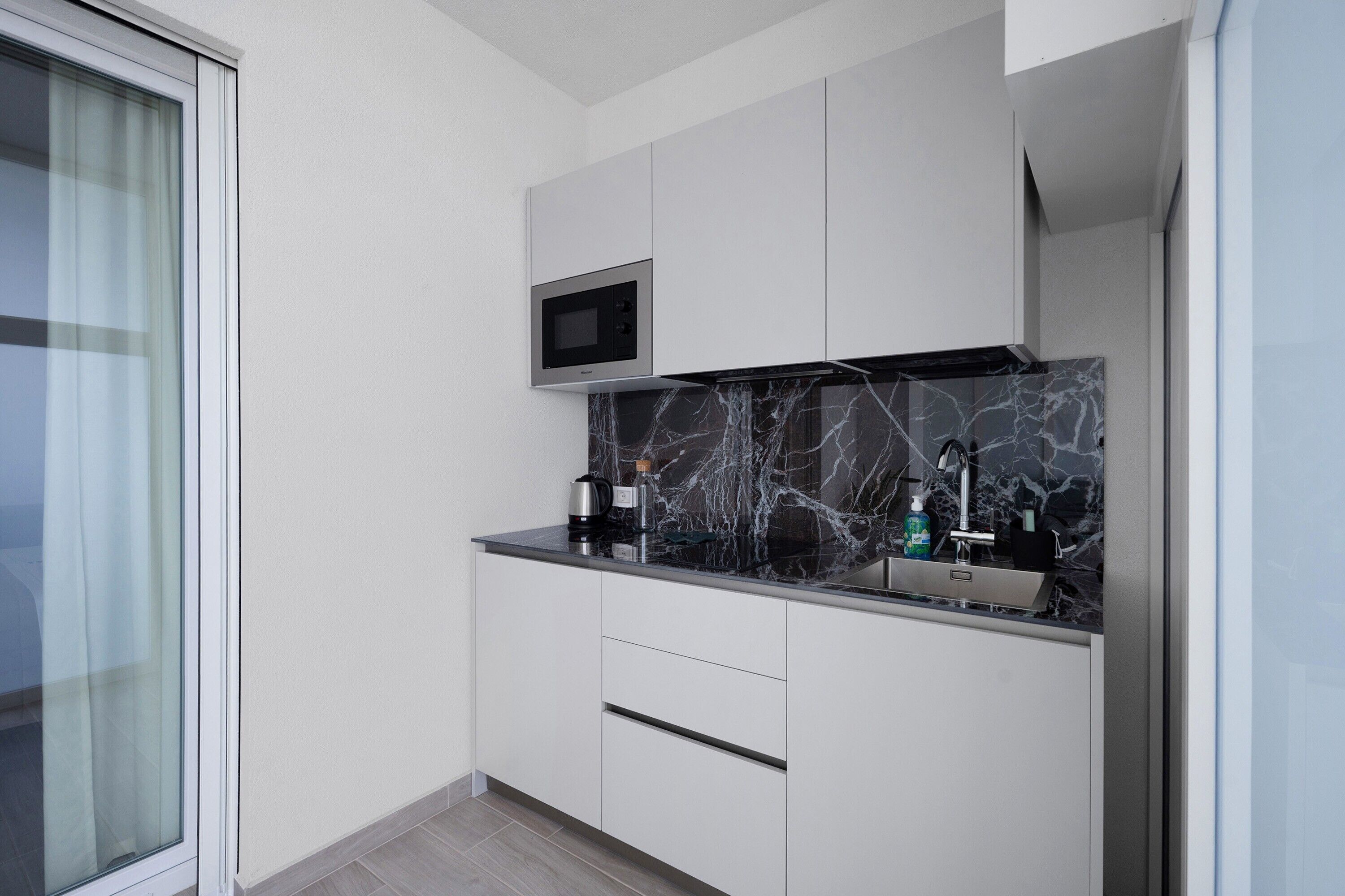 Una cucina moderna con forno a microonde integrato, zoccolo in marmo e lavello in acciaio inossidabile.