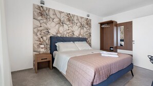 A bedroom with a bed, a nightstand, a wooden wardrobe, a mirror, and a wall with a floral pattern. - Apartment 'U Gnore - Polpo Room' with Sea View, Wi-Fi and Air Conditioning (Bari)