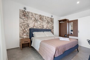Ein Schlafzimmer mit einem Bett, einem Nachttisch, einem Holzschrank, einem Spiegel und einer Wand mit floralem Muster.