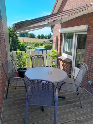 Eine Terrasse mit einem runden Tisch und Stühlen, einem Blumentopf und Blick auf ein Backsteingebäude.