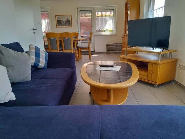Ein Wohnzimmer mit einer Couch, einem Couchtisch, einem Fernseher auf einem Schrank und einem Essbereich im Hintergrund.