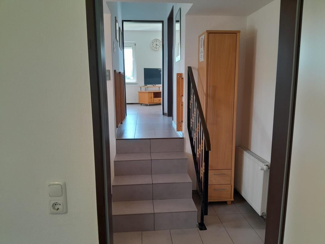 A staircase leading to a room with a radiator, a wooden cabinet, and a view into another room with a radiator and a clock.