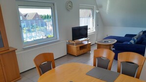 Een woonkamer met een televisie, bank, eettafel en stoelen.