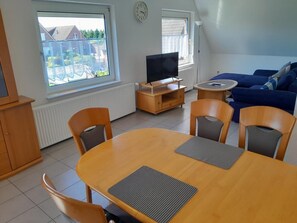 A living room with a TV, sofa, dining table, and chairs. - NEW! Vacation Rental "Sound of the Sea" 4c (Dornum)