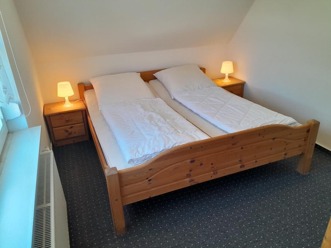Una cama individual con estructura de madera, dos mesitas de noche con lámparas y un radiador en la pared.