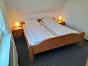 Ein Einzelbett mit Holzrahmen, zwei Nachttische mit Lampen und ein Heizkörper an der Wand.